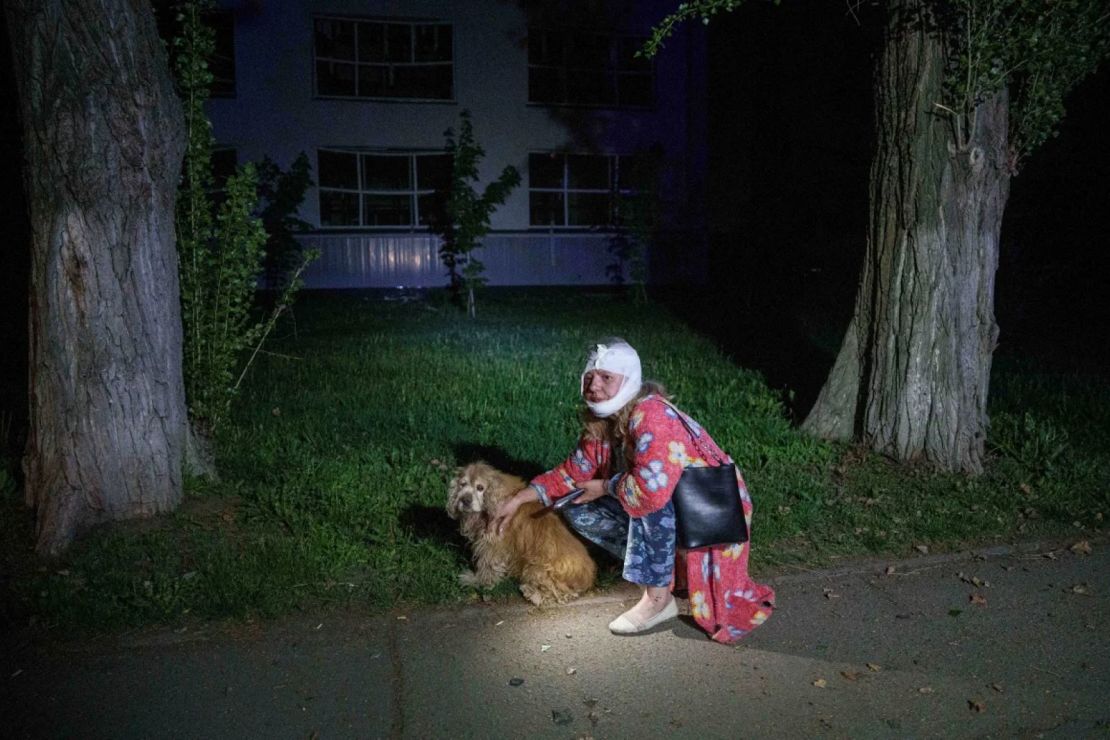 Una mujer herida se sienta con su perro cerca de una casa destruida por un ataque aéreo ruso.