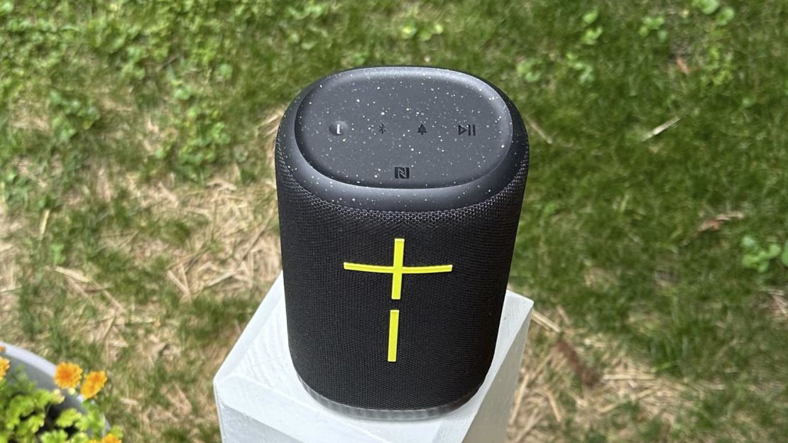 UE Everboom speaker sitting on a white pillar surrounded by green grass.