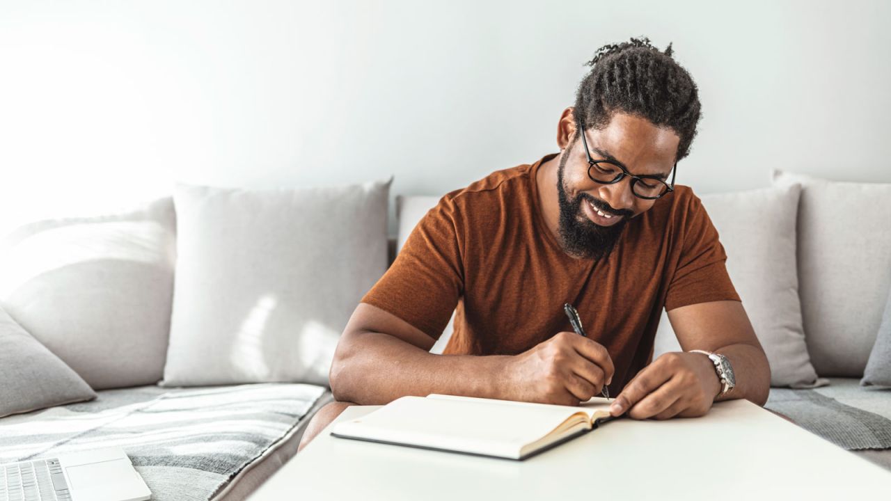 black man writing in book budgeting