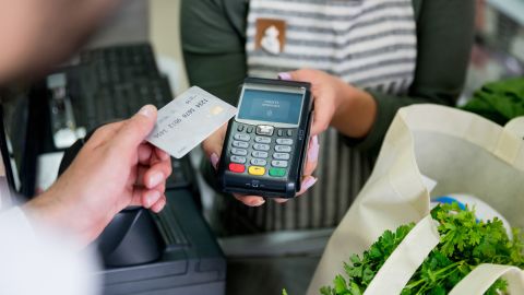 A person holding a credit card above a contactless credit card terminal.