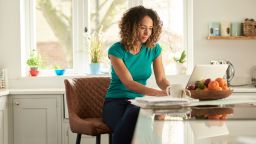 woman at kitchen counter on laptop budgeting