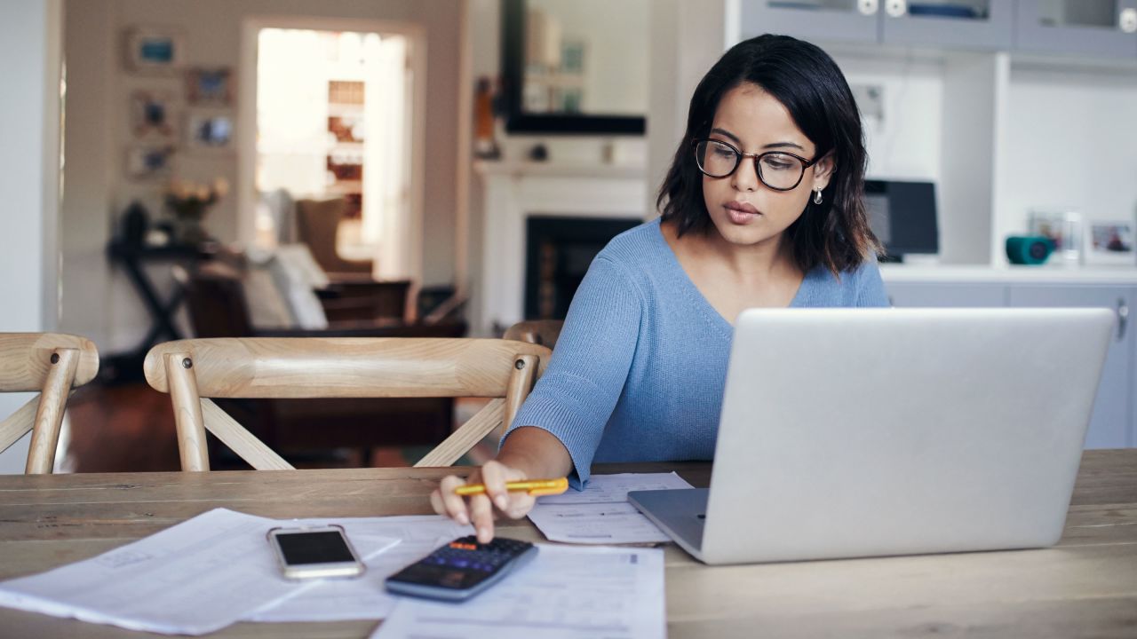 Woman with calculator, laptop and a smartphone sitting at a table.