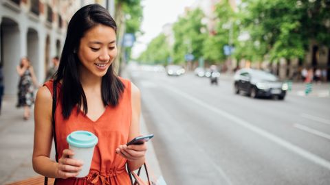 woman with coffee cup looking at banking phone app