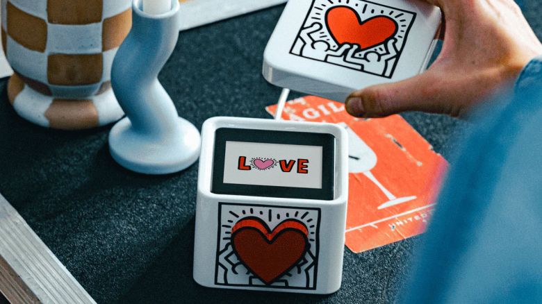 A hand removes the lid of a small white box to reveal a screen that reads "Love."