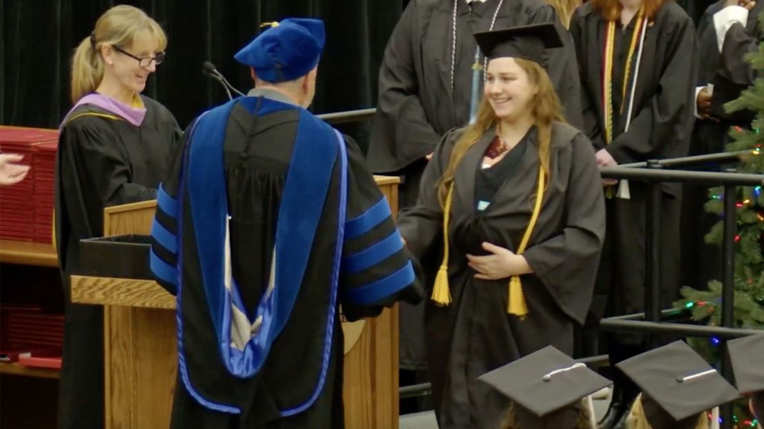 Grace Szymchack smiles as she receives her degree while holding baby Annabelle.