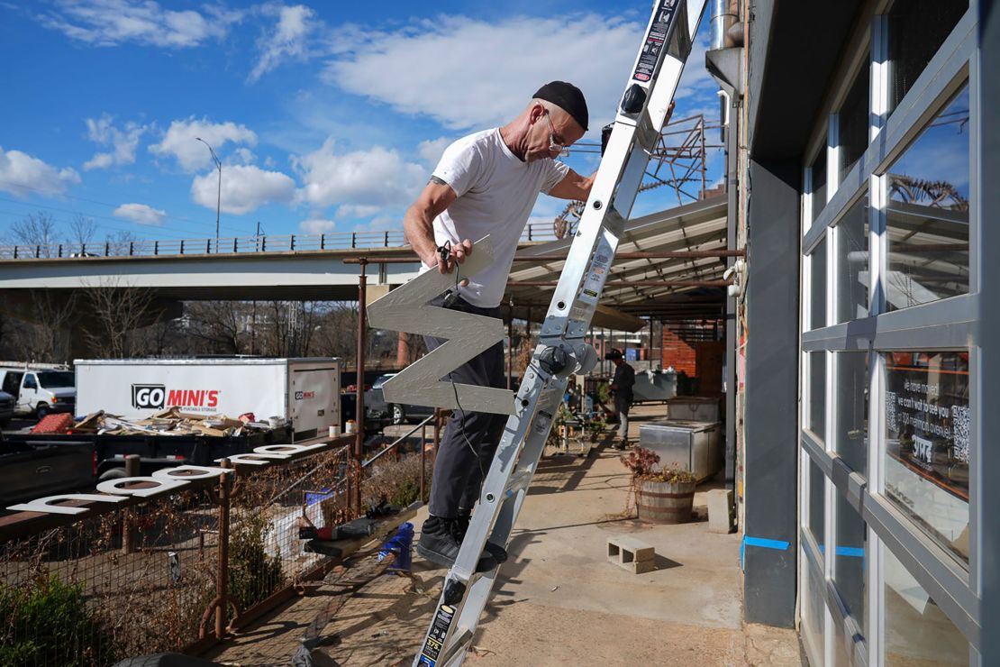 Dec 18, 2024; Asheville, North Carolina, USA; Larry Hopkins of Ananda Hair Studio takes down signage for his store. Hopkins said he had been in the River Arts District location for 13 years before he had to move his store due to flooding by Helene.