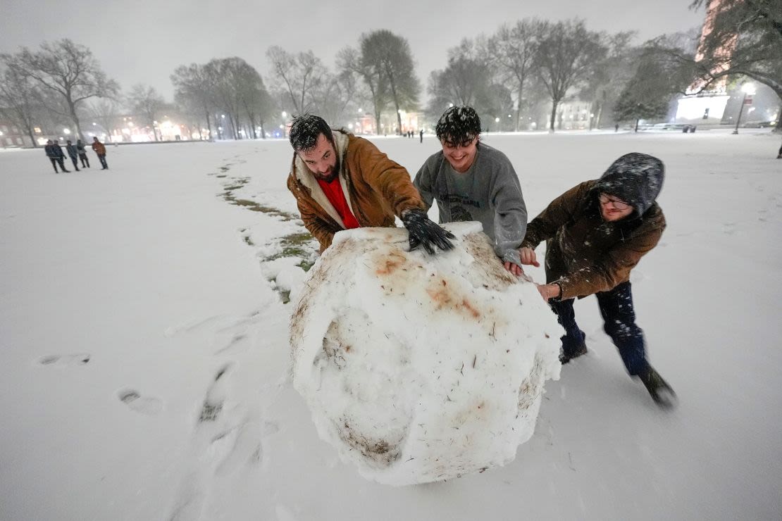 Estudiantes de la Universidad de Alabama, en Tuscaloosa, luchan por hacer rodar una enorme bola de nieve mientras se preparan para construir un muñeco de nieve antes del amanecer del viernes.