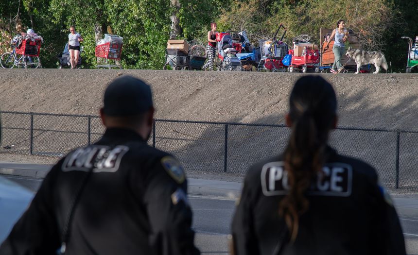 Stockton Police officers watch as inhabitants of a homeless encampment on an island on White Slough move their possessions onto a levee along Trinity Parkway near McAuliffe Road in north Stockton, California, on July 22, 2025. Inhabitants of the camp were evicted by city, county and state agencies.