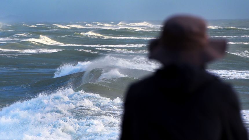 A man watches the waves from the pier in Daytona Beach on August 20, 2025, as Hurricane Erin passes offshore.