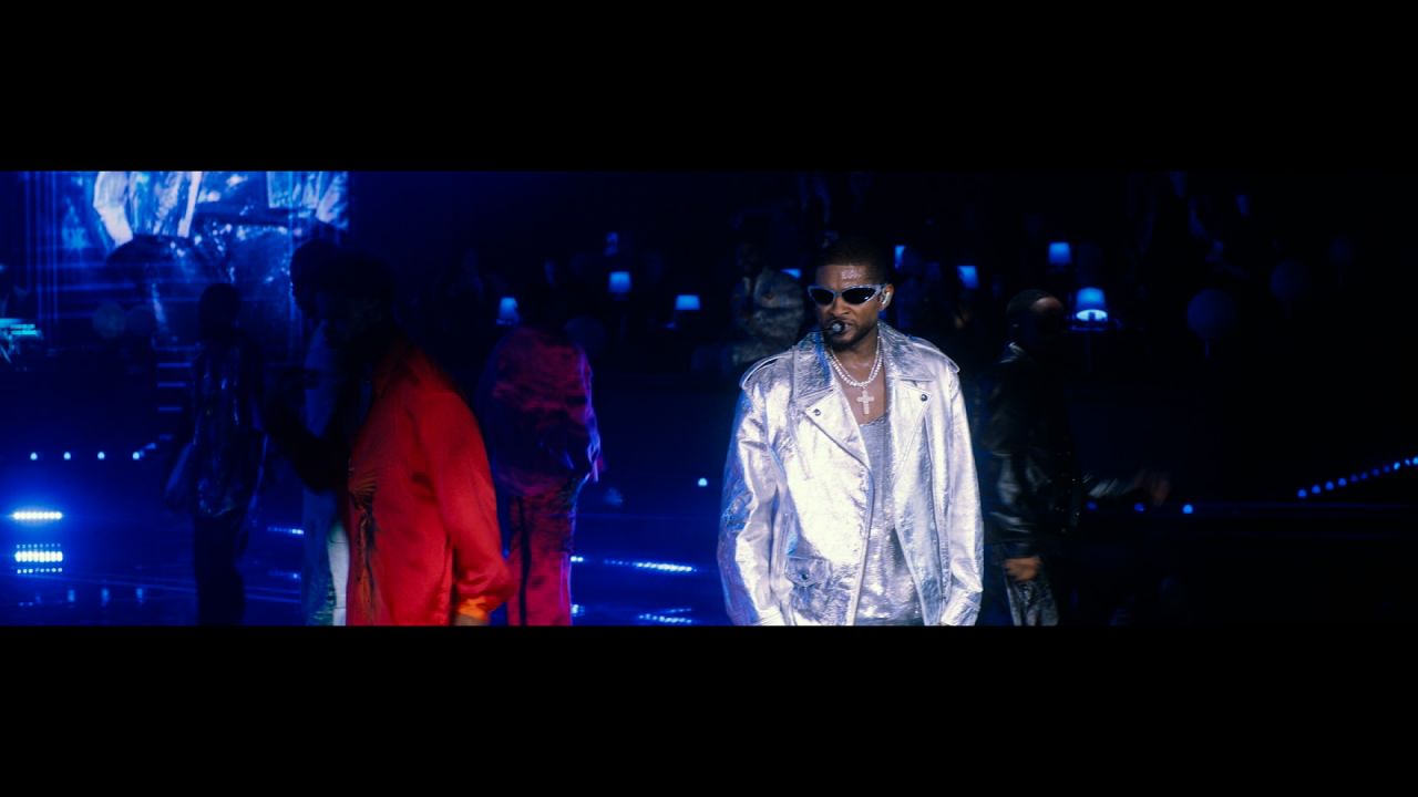 Usher, on stage wearing shades and a silver jumpsuit, sings as he's surrounded by male dancers.