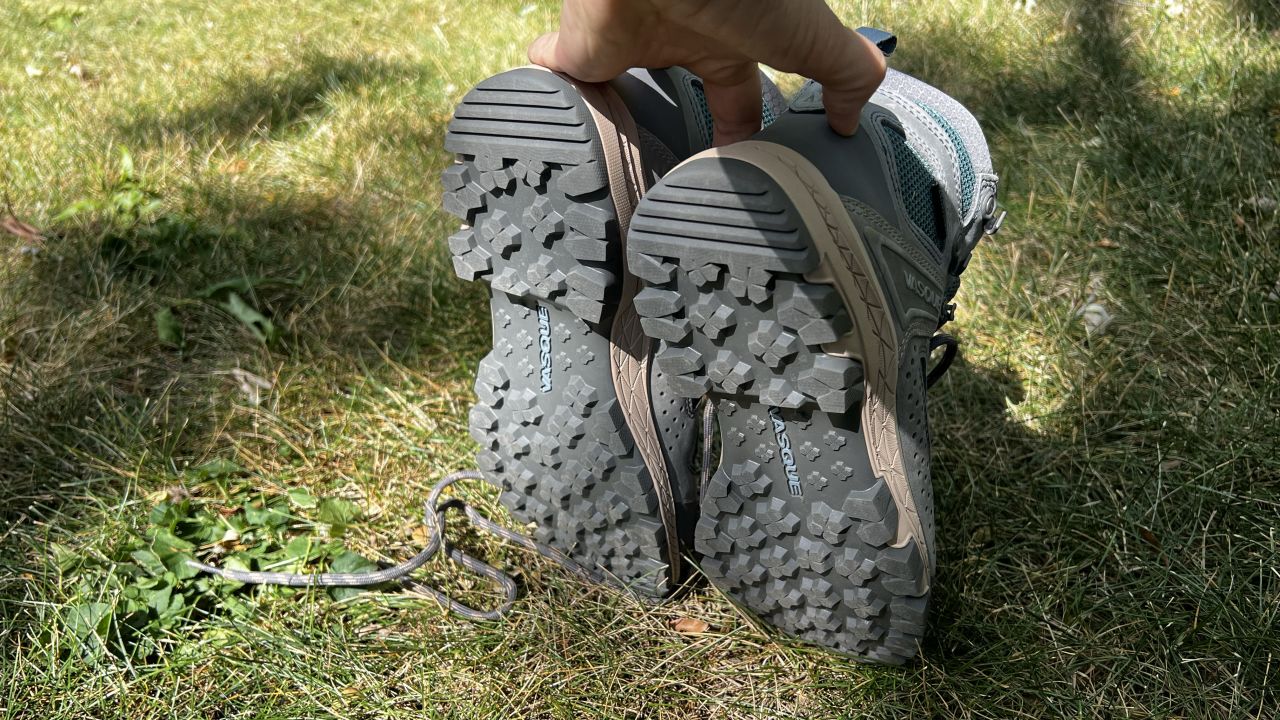 The bottom of a pair of hiking boots are held above a patch of grass.