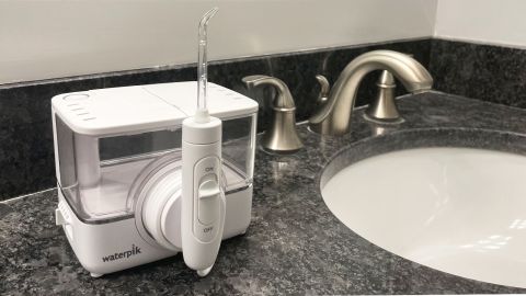 The Waterpik ION water flosser on a marble bathroom counter, next to a sink.