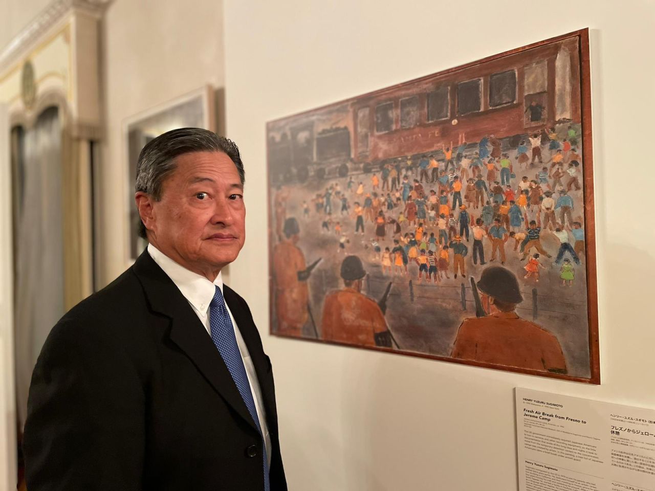 Vice chair of the Japanese American National Museum, Robert T. Fujioka, stood beside Henry Sugimoto's "Fresh Air Break from Fresno to Jerome Camp," a painting depicting the camp where Fujioka's own mother and grandfather were incarcerated.