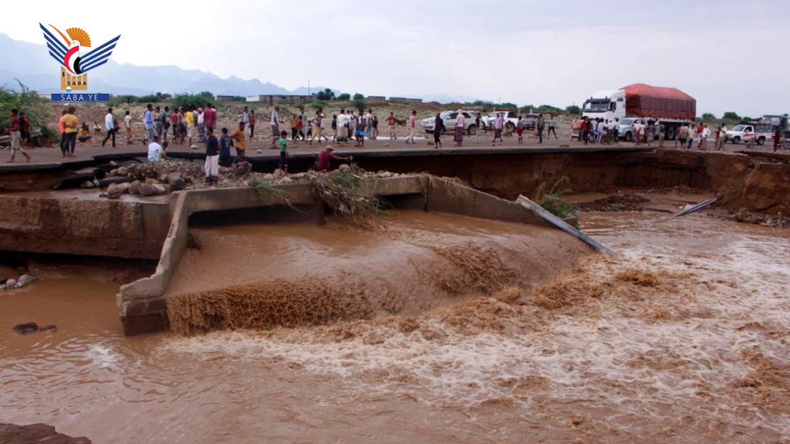 People traverse a road damaged in recent flooding.