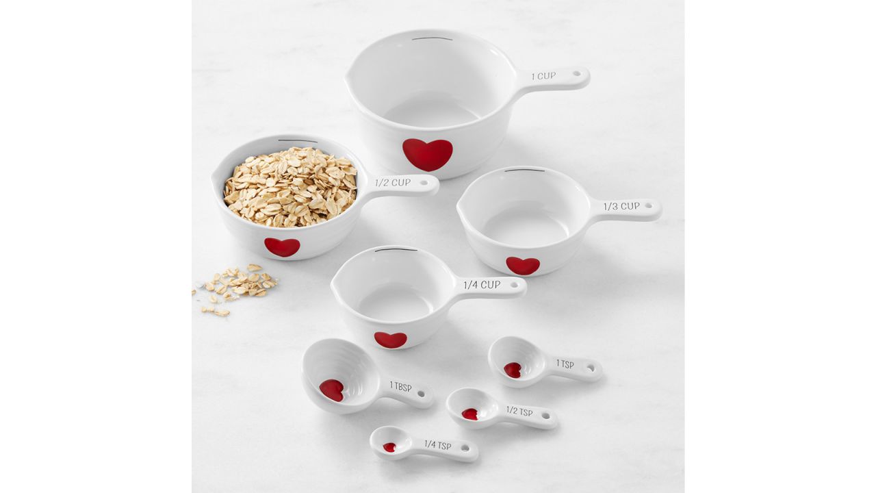 White measuring cups and spoons, each with a painted red heart.