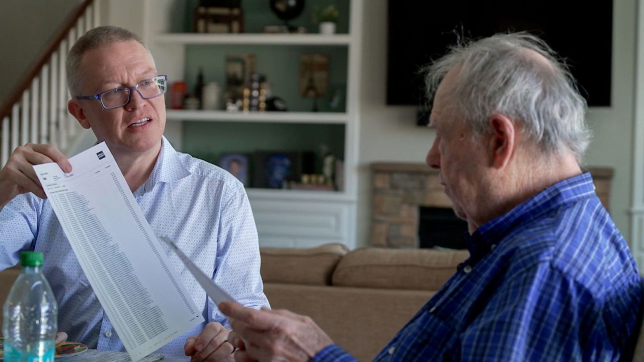 Richard Benjamin, right, and his son Jason look at bank statements showing more than 100 donations that Benjamin made to WinRed in a single day. (CNN)