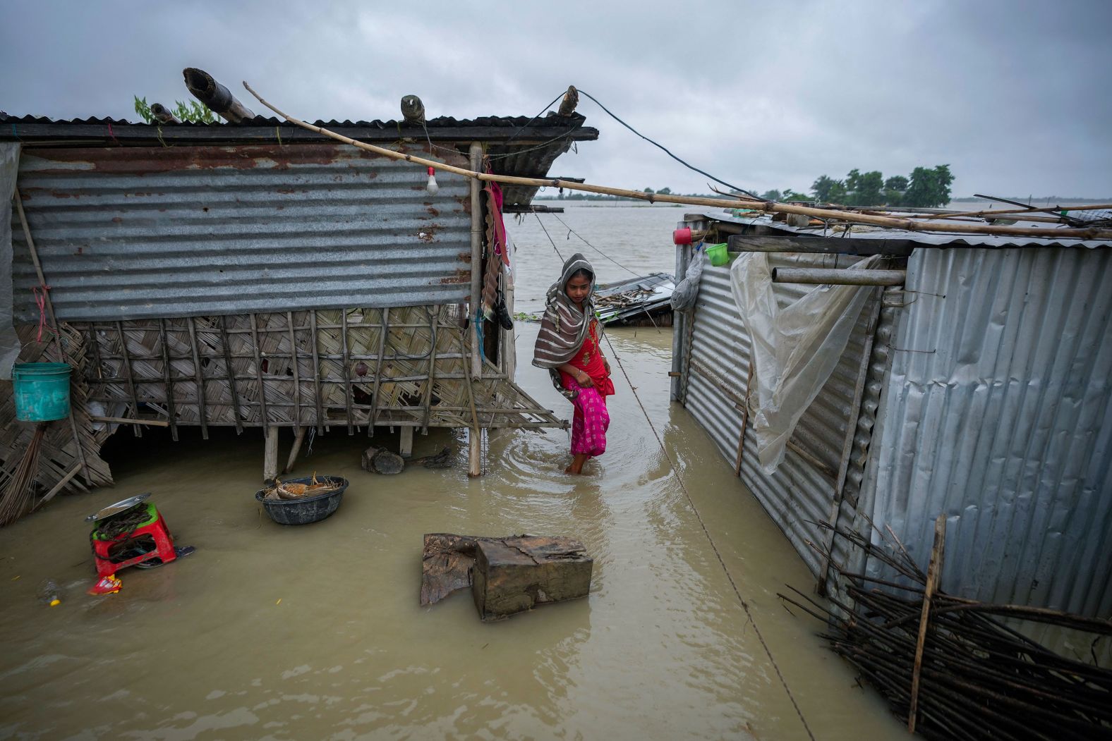 A woman wades through floodwaters near her submerged house in the Indian village of Sildubi on Tuesday, July 2. Floods and landslides have been triggered by heavy rains in India's northeast.