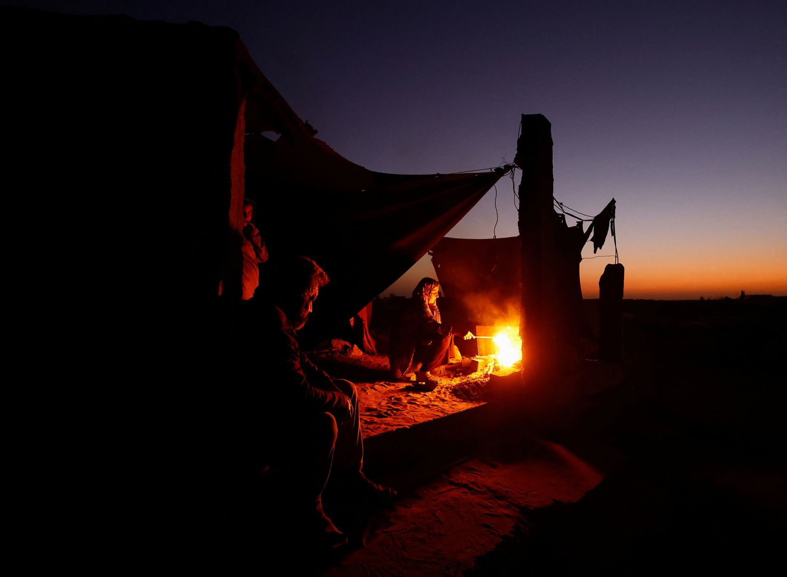 Displaced Palestinians light a fire next to their tent as they camp at a cemetery in Khan Younis, Gaza, on Sunday, October 27.