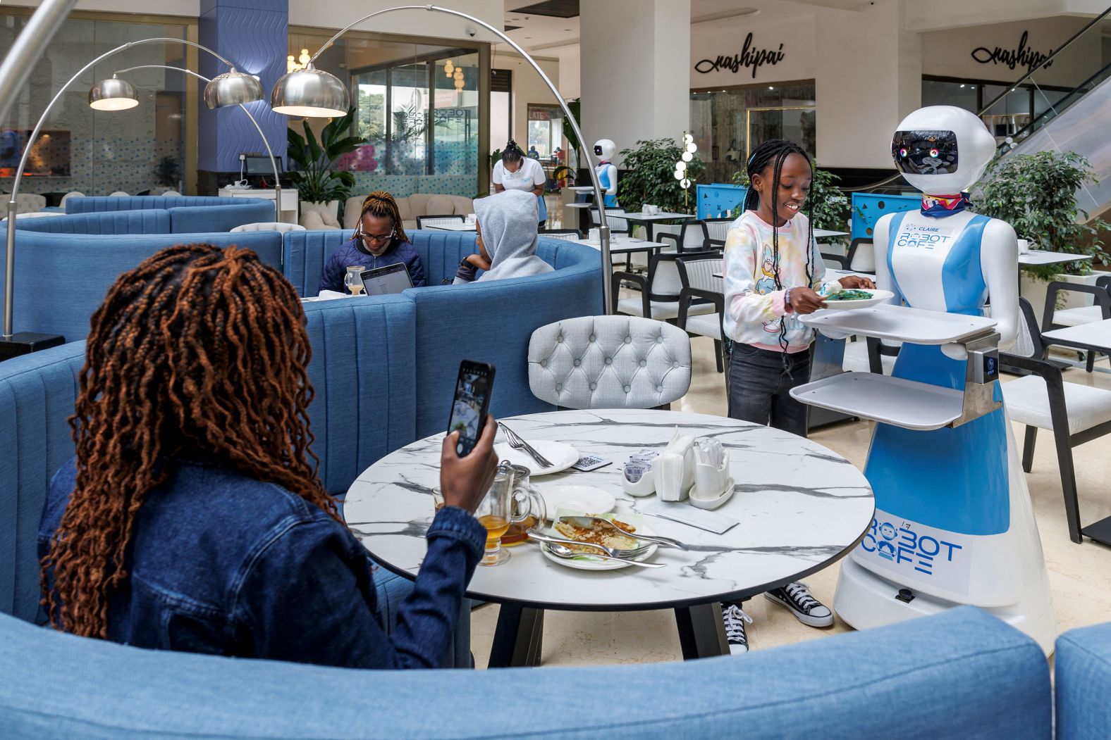 A young patron receives her meal from a robotic waiter at the Robot Cafe in Nairobi, Kenya, on Tuesday, August 27.