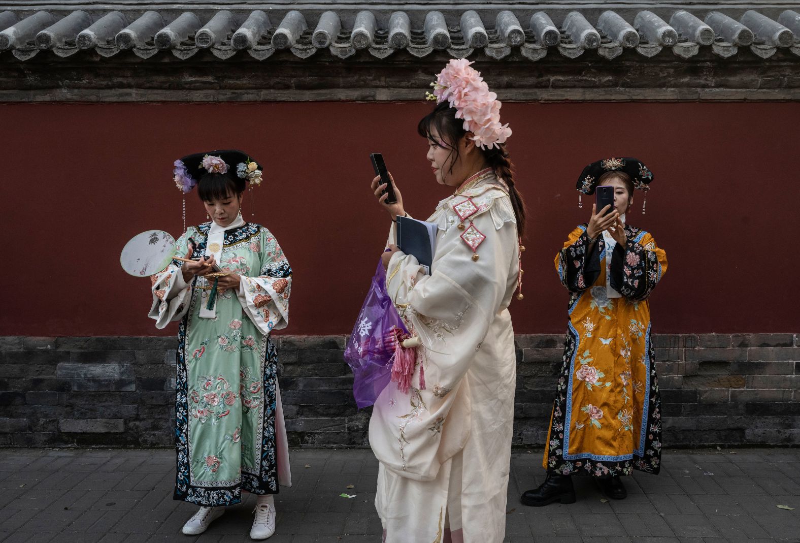 Women wearing traditional dress look at their cell phones as they visit a historic Beijing neighborhood during the Golden Week holiday on Thursday, October 3.