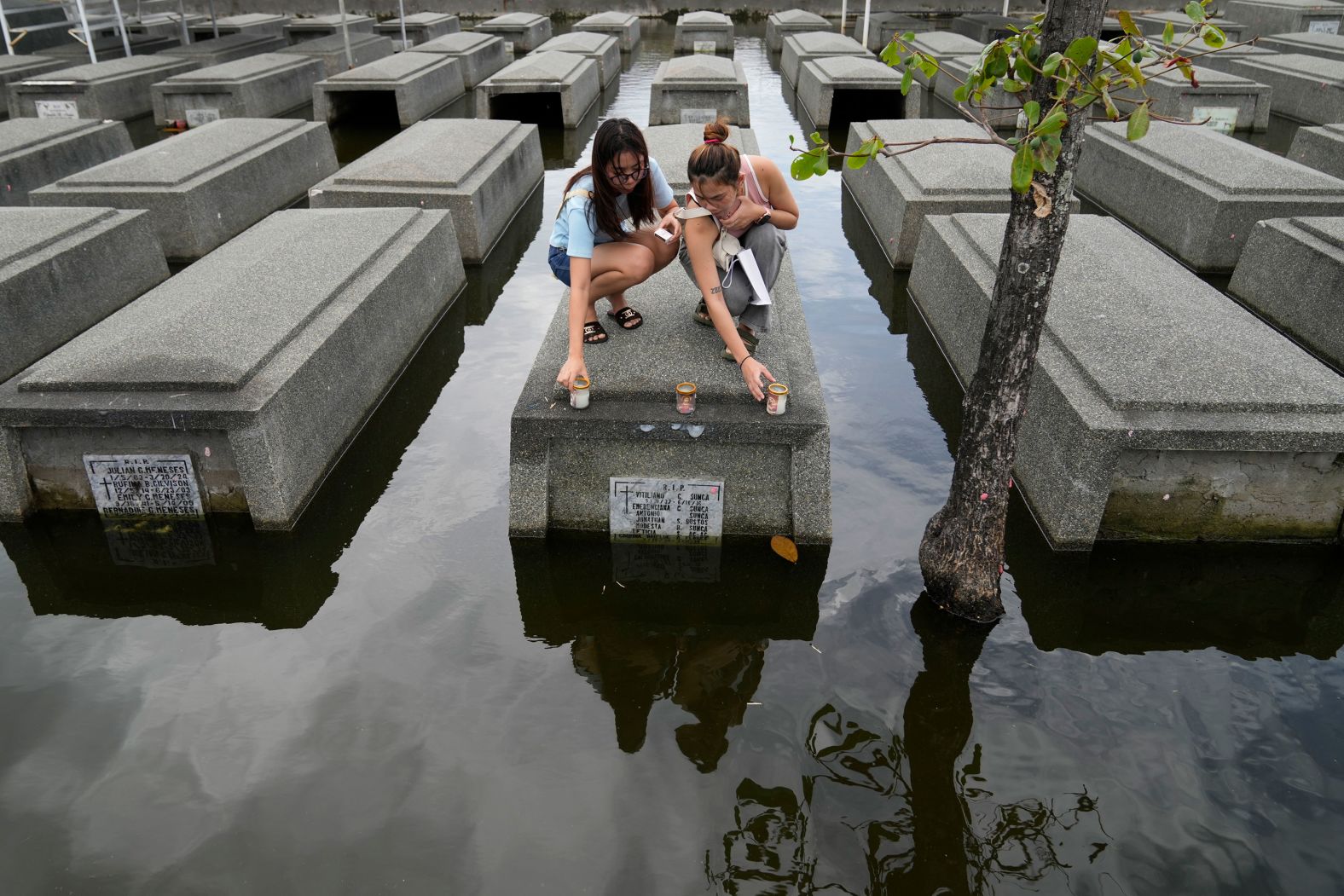 Women place candles on the half-submerged tomb of family members in Masantol, Philippines, on Thursday, October 31. <a href="index.php?page=&url=https%3A%2F%2Fwww.cnn.com%2F2024%2F10%2F28%2Fclimate%2Fphilippines-storm-trami-kristine-intl-hnk%2Findex.html">Tropical Storm Trami</a>, known locally as Kristine, swept across the northeastern Philippines last week, inundating entire towns with severe flooding.