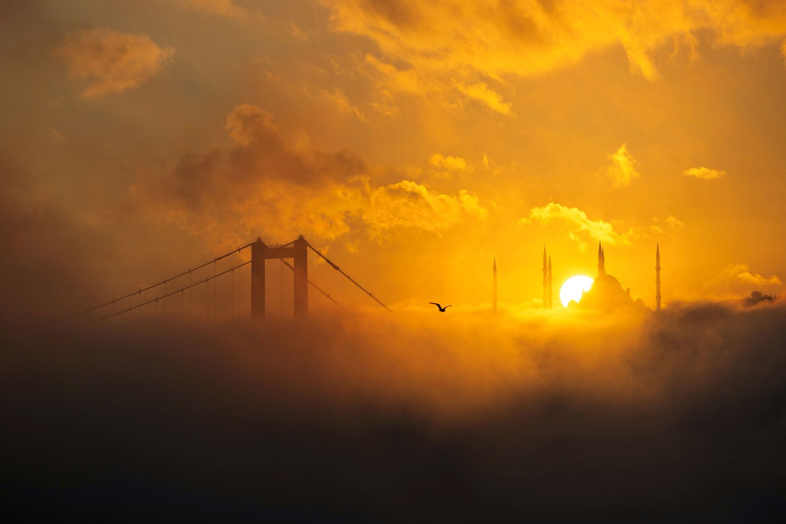 The sun rises behind the Grand Çamlıca Mosque as the Bosphorus Bridge is covered in fog in Istanbul on Wednesday, October 16.