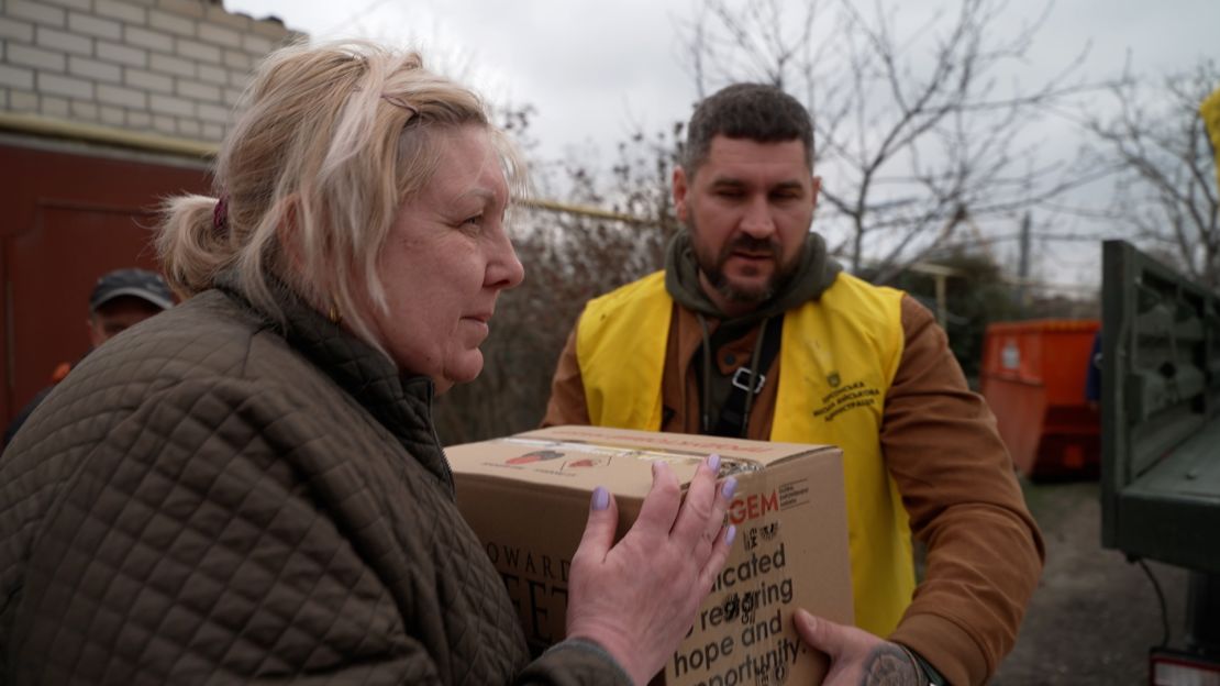 A woman accepts a box of food before hurrying back into the safety of her house.