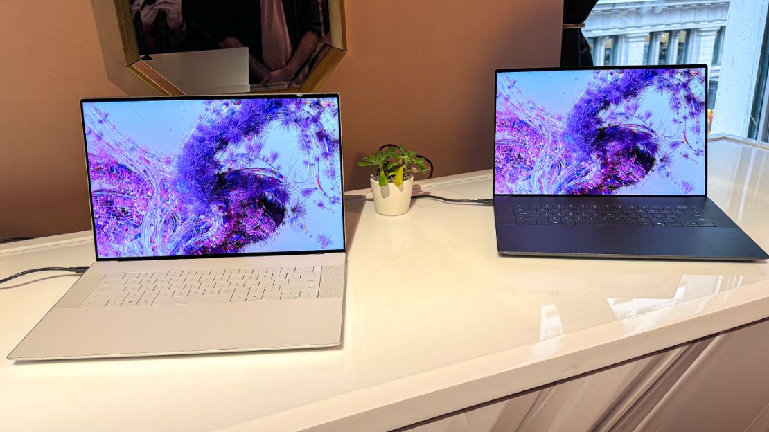 Two laptops on a white table. Each is displaying purple shapes on its screen.