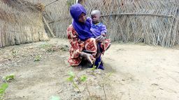 Yagana Usman gestures toward her infant twin's grave while holding her surviving son in her arms at the Fulatari camp for internally displaced persons in Borno, northeastern Nigeria, on September 5, 2025.