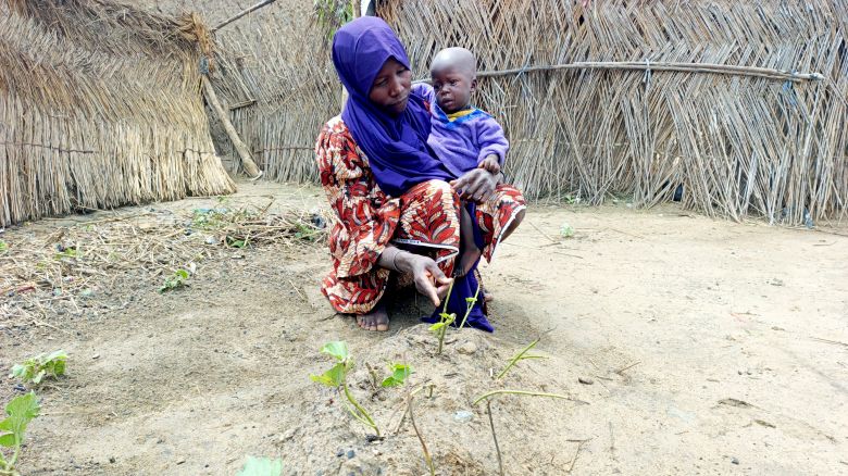 Yagana Usman gestures toward her infant twin's grave while holding her surviving son in her arms at the Fulatari camp for internally displaced persons in Borno, northeastern Nigeria, on September 5, 2025.