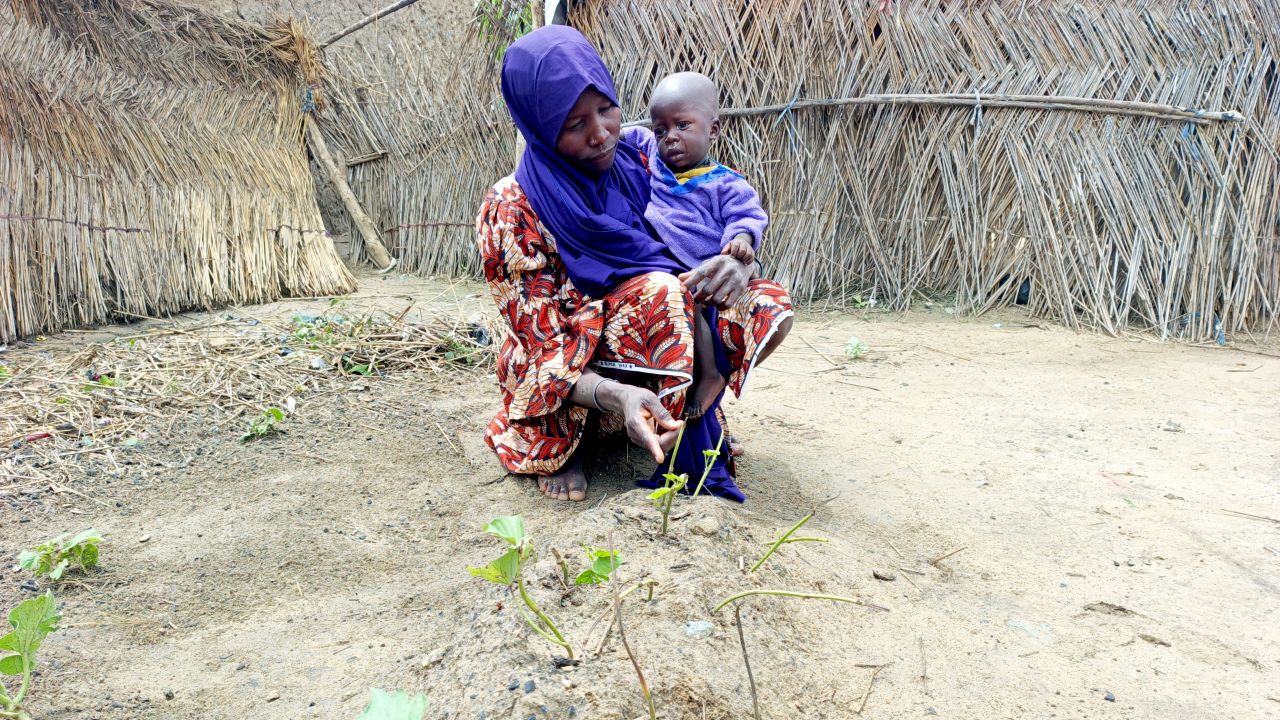Yagana Usman gestures toward her infant twin's grave while holding her surviving son in her arms at the Fulatari camp for internally displaced persons in Borno, northeastern Nigeria, on September 5, 2025.