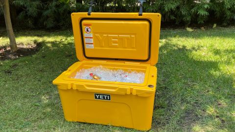 A yellow Yeti Tundra 45 cooler in a grassy yard, turned on, filled with ice cubes and cans of soda.